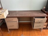 Front view of beige/tan metal desk with wood top, drawers visible, wear on surface
