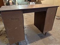 Desk backside showing particleboard panel marked "WALNUT" and metal legs