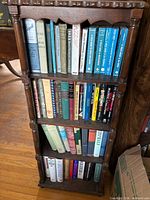 Full view of narrow four-shelf bookcase filled with assorted hardcover books