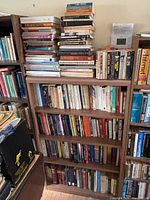 Tall bookshelf and stacked books displaying quantity and variety of formats and subjects