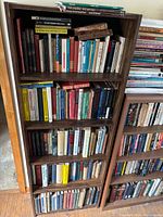 Front view of five-shelf wooden bookcase filled with assorted reference, science, history, language and programming books in mixed hardcover and paperback formats