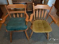 Two wooden dining armchairs with spindle backs, armrests, and different colored cushions
