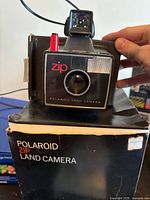 Front view of Polaroid Zip Land camera on top of its original box with flash/viewfinder attached