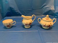 Teacup, creamer and covered sugar bowl arranged side by side showing pattern and condition