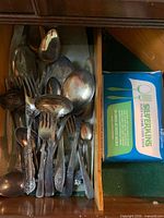 Drawer with assorted tarnished silver-plated spoons, forks, ladle and box of anti-tarnish tissue cloth