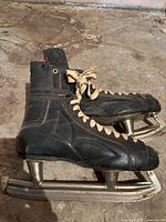 Side view of black leather figure skates showing laces, stitching detail, and metal figure blades with toe picks