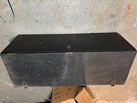 Closed black painted wooden trunk front view with latch and metal brackets