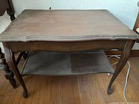 Front view of entire side table showing scalloped top, lower shelf, curved legs and wear
