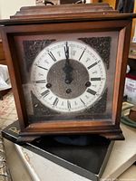 Front view of mahogany mantel clock showing dial, brass filigree accents, glass cover, wood case