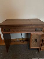 Front view of the closed sewing cabinet showing veneer finish, drawer, and side door