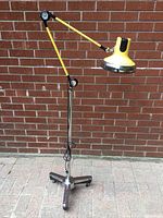 Full view of yellow articulated floor lamp on five-caster chrome base