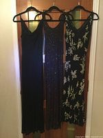Three gowns on hangers: plain black, fully beaded, and black with white bead floral
