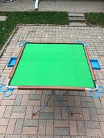 Full view of Mahjong table top showing green surface, brown edge, blue drink holders, folding legs