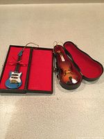 Open cases showing violin and blue guitar ornaments inside red-lined interiors