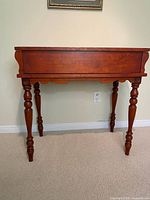 Front view of cherry writing desk showing hinged top, turned legs, scalloped apron