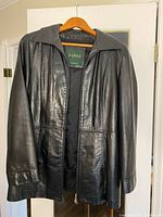 Front view of black leather jacket on hanger showing collar, zipper and overall length