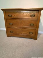 Front view showing three drawers, hardware, feet