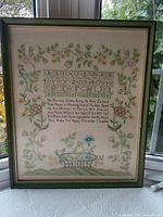Full view of framed needlepoint sampler under glass