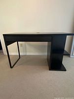 Full view of black-brown IKEA MICKE desk, drawer closed, shelves visible