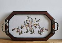 Full view of tray showing wood frame, metal handles and embroidered center