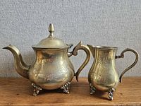Teapot and creamer side by side showing engraving and claw feet