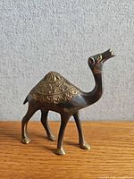 Side view of brass and bronze camel figurine showing engraved saddle