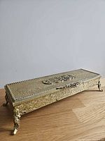 Closed rectangular brass casket on cabriole legs showing ornate exterior and central medallion