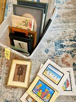 Plastic bin with multiple framed artworks and loose prints