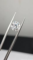 Round brilliant moissanite held by tweezers