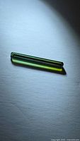 Elongated green tourmaline gemstone top view under direct light