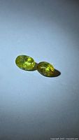 Two oval faceted chartreuse sphene gemstones on neutral background