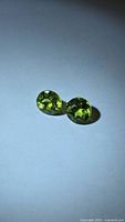 Pair of round apple green peridot gemstones on neutral background