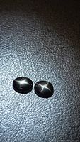 Both black star diopside cabochons showing star effect on textured background