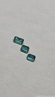 Three rectangular emerald-cut gemstones on light background