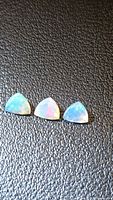 Three faceted trillion opals on black textured background showing play-of-colour