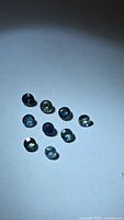 Ten small round faceted sapphires arranged on white background, showing overall lot