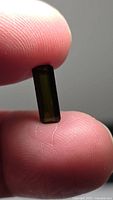 Rectangular olive-green tourmaline held between fingers, showing body color and cut