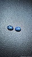 Pair of blue star sapphire cabochons on textured background showing six-ray star