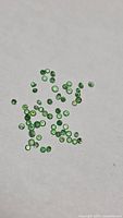 Scattered loose green faceted tsavorite garnets on white background