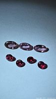 Three oval pink-purple sapphires and four round red rubies on light background