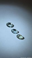 Three light green oval-cut tourmalines on white background