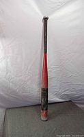 Full view of red and black aluminum baseball bat standing vertically
