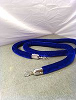 Blue velvet stanchion rope coiled, showing silver-tone hooks