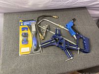 All tools laid out: packaged scraper set, four blue corner clamps, air blow gun, torch hose