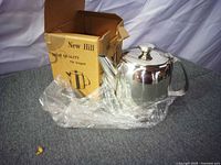 Stainless steel teapot partially wrapped in plastic beside original New Hill box