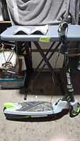 Full view of scooter folded next to ironing board, manual placed on board
