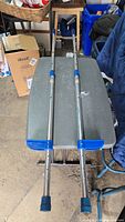 Full view of both aluminum stilts on table showing blue foot platforms and adjustment collars