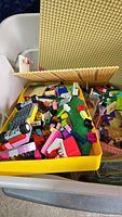 Bin with yellow tray of assorted LEGO parts and tan baseplate