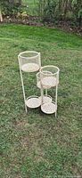 Full view of cream metal plant stand with six circular mesh holders on lawn