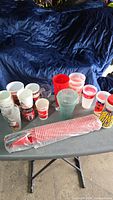 Overview of assorted Coca-Cola cups and sealed red cup sleeve on table